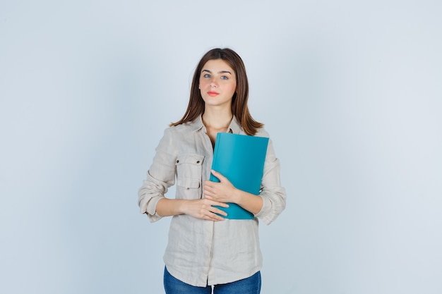 Retrato de linda chica sosteniendo la carpeta en camisa y mirando confiado