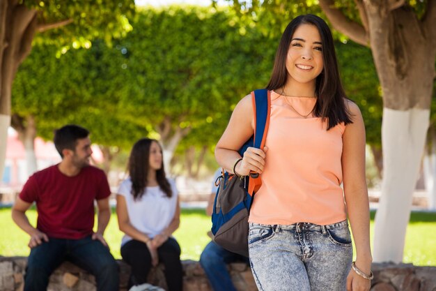 Retrato de una linda chica en la universidad que lleva una mochila escolar con un grupo de amigos en el fondo