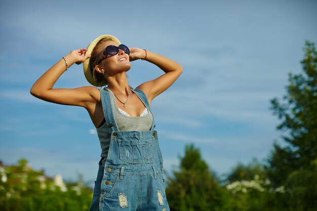 Retrato de linda divertida joven elegante mujer sonriente mujer modelo en tela casual moderno con cuerpo perfecto bronceado al aire libre en el parque con sombrero