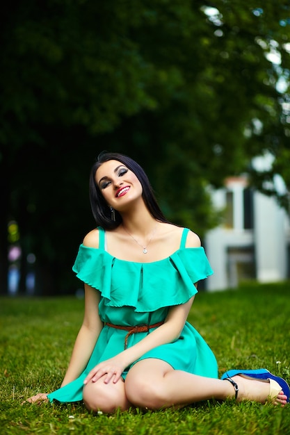 Retrato de linda divertida sexy joven elegante mujer sonriente modelo de niña en vestido verde moderno brillante con cuerpo perfecto bronceado al aire libre en el parque