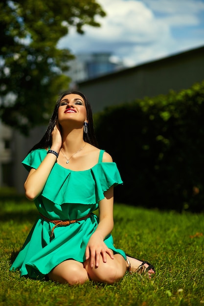 Retrato de linda divertida sexy joven elegante mujer sonriente modelo de niña en vestido verde moderno brillante con cuerpo perfecto bronceado al aire libre en el parque