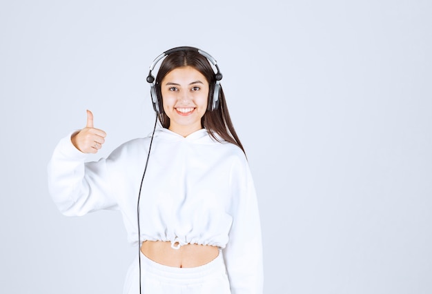 Retrato de una linda joven modelo con auriculares mostrando un pulgar hacia arriba.