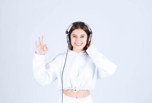 Retrato de una linda joven modelo con auriculares mostrando signo de silencio.