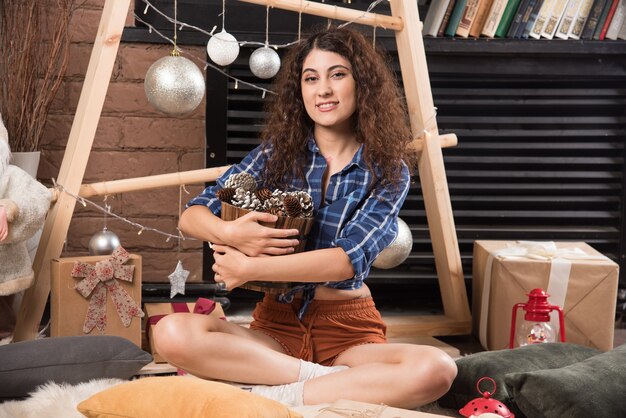 Retrato de una linda joven sosteniendo una canasta de madera de piñas