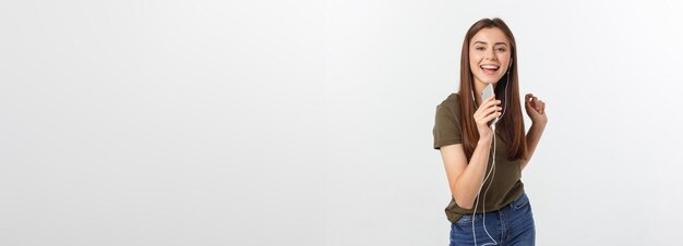 Retrato de una linda mujer alegre escuchando música en auriculares y bailando aislada en una espalda blanca