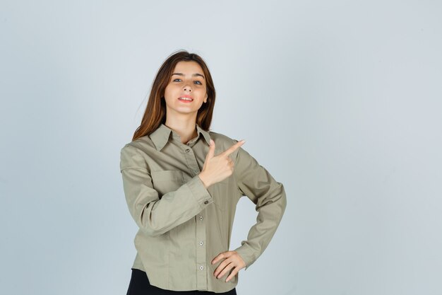 Retrato de linda mujer joven apuntando a la esquina superior derecha en camisa y mirando orgullosa vista frontal