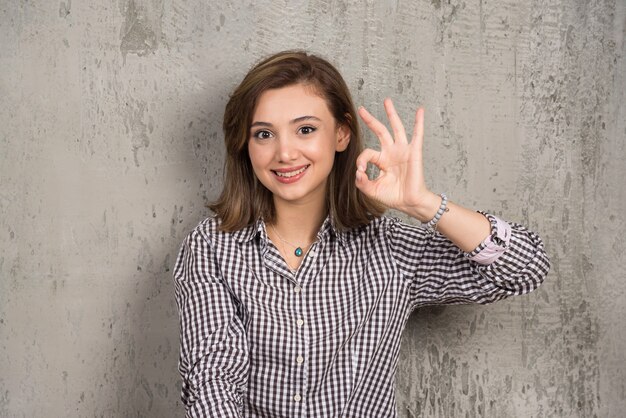 Retrato de una linda mujer joven que muestra el signo de ok con los dedos y mirando al frente