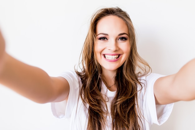 Retrato de una linda mujer sonriente haciendo foto selfie en smartphone aislado sobre un fondo blanco.