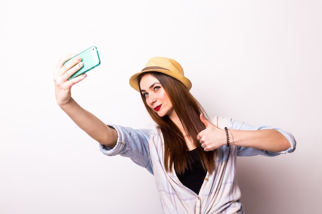 Retrato de una linda mujer sonriente haciendo foto selfie en smartphone en un blanco