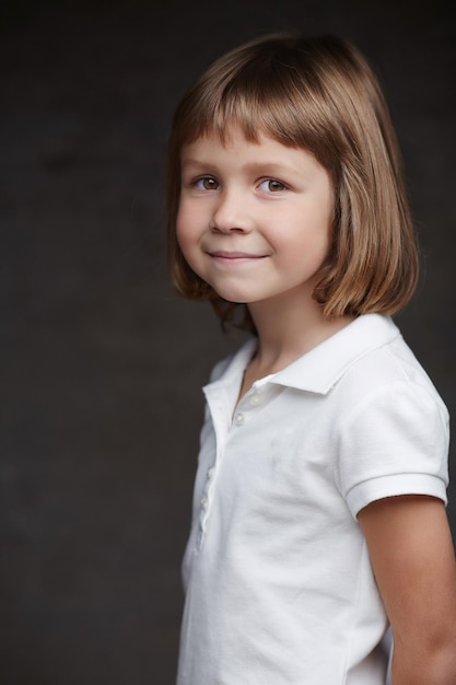 Retrato de una linda niña con una camisa blanca aislada en un fondo gris oscuro.