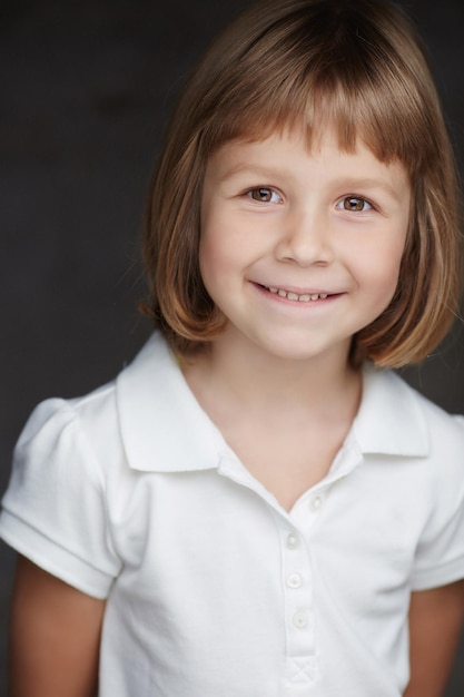 Retrato de una linda niña con una camisa blanca aislada en un fondo gris oscuro.