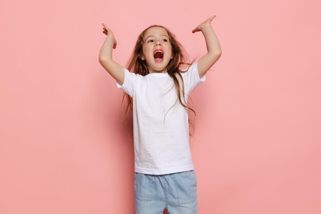 Retrato de una linda niña emotiva posando gritando aislada sobre el fondo rosa del estudio