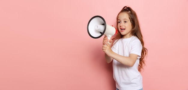 Retrato de una linda niña gritando en un megáfono posando aislada sobre el fondo rosa del estudio