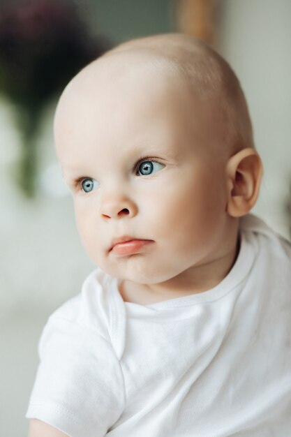 Retrato de lindo bebé con pelo corto se ve a un lado en la habitación luminosa