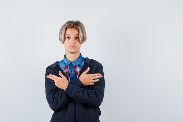 Retrato de lindo muchacho adolescente mostrando gesto de pistola en camisa, sudadera con capucha y mirando pensativo vista frontal