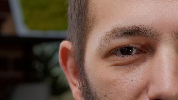 Retrato macro de un modelo masculino que muestra un ojo en la cámara, tiene ojos marrones y sonríe. Joven con aspecto auténtico y visión saludable, con expresiones faciales positivas. De cerca.