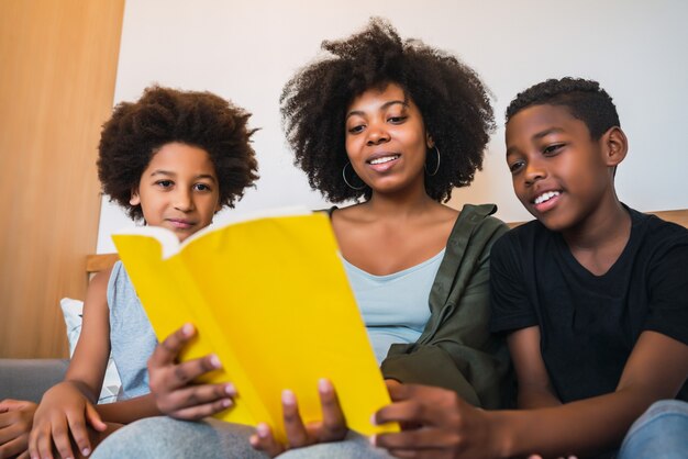 Retrato de madre afroamericana leyendo un libro a sus hijos en casa. Concepto de familia y estilo de vida.