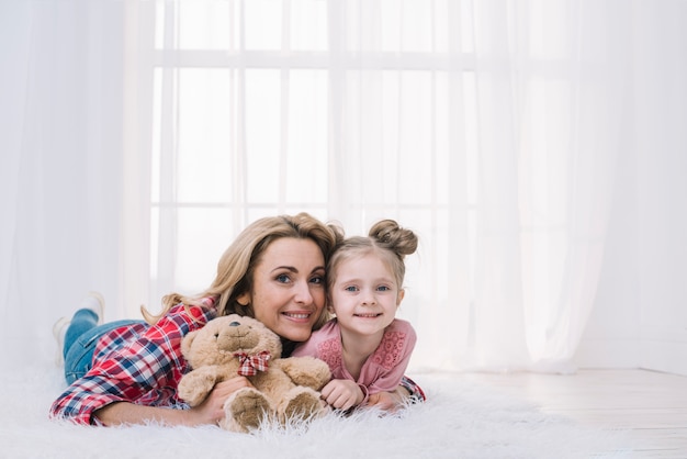 Foto gratuita retrato, de, madre e hija, acostado, en, piel, tenencia, osito de peluche