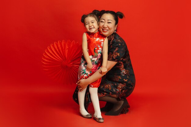 Retrato de madre e hija asiática aislado en la pared roja en vestimentas tradicionales