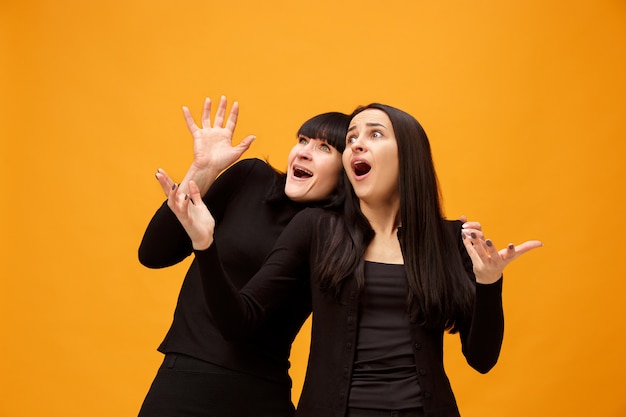 Retrato de una madre e hija asustadas en el estudio sobre fondo dorado. Colores de moda. Concepto de expresiones faciales y emociones positivas humanas