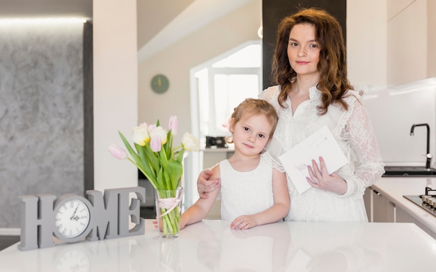 Retrato de madre e hija de pie cerca de la mesa de comedor blanco