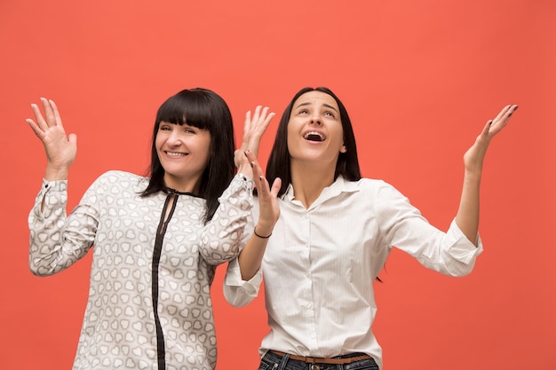 Un retrato de una madre e hija sorprendidas en el estudio sobre fondo de coral vivo. Colores de moda. Concepto de expresiones faciales y emociones positivas humanas