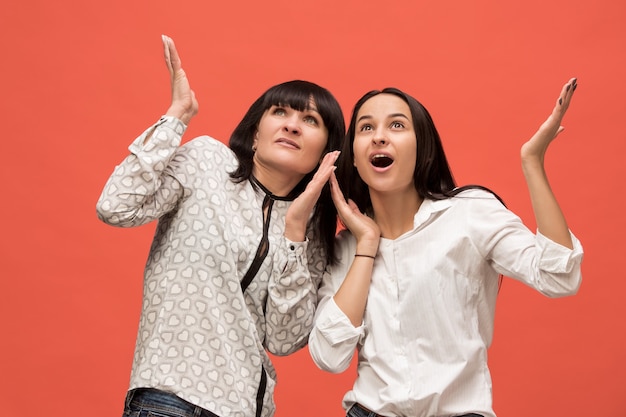 Un retrato de una madre e hija sorprendidas en el estudio sobre fondo de coral vivo. Colores de moda. Concepto de expresiones faciales y emociones positivas humanas