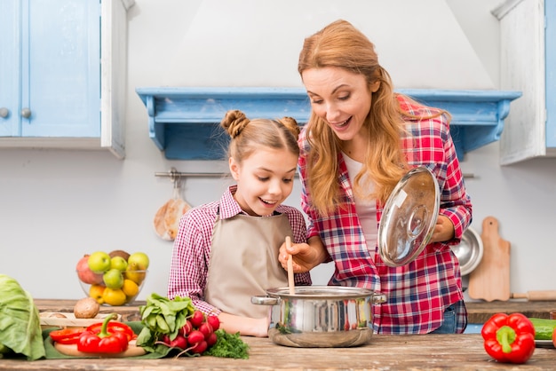 Foto gratuita retrato de una madre y una hija sonrientes mirando comida preparada en mesa de madera