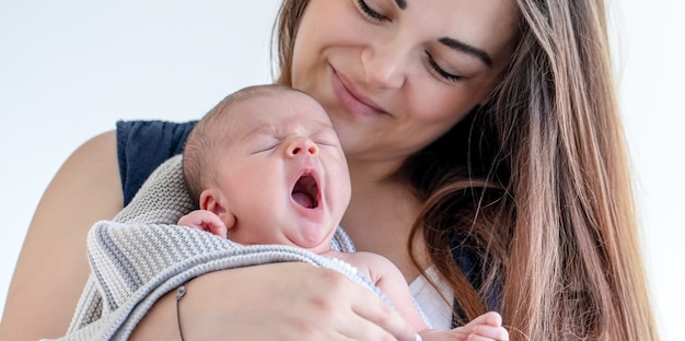 Retrato de una madre con un hijo recién nacido soñoliento sobre un fondo blanco.