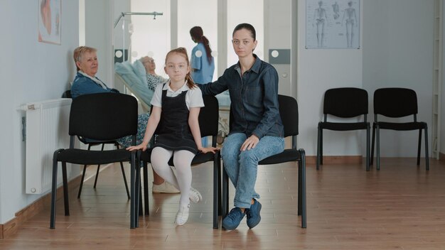 Retrato de madre y niña en la sala de espera de la clínica. Mujer con un niño sentado en el vestíbulo de recepción, esperando para ir a una cita médica y una visita de control anual con un médico.