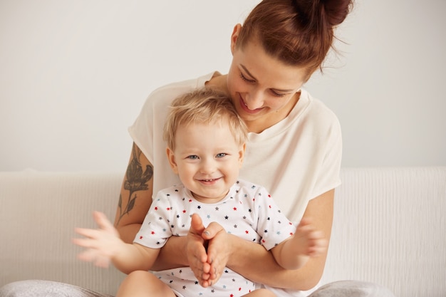 Retrato de madre pelirroja divirtiéndose con su hijo rubio interior con niño pequeño mirando a la cámara