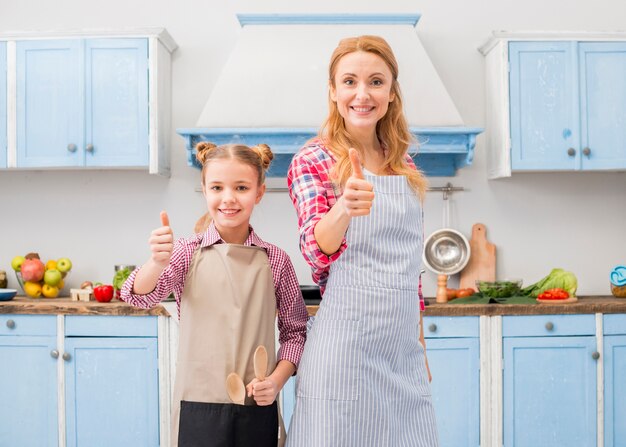 El retrato de una madre sonriente y su hija mostrando el pulgar arriba firman en la cocina