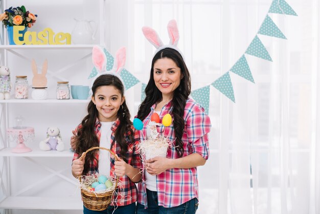 Retrato de la madre y su hija con orejas de conejo con coloridos huevos de Pascua en la mano