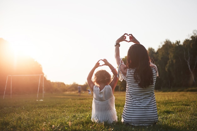 El retrato de una madre y su niña conforman su corazón en el parque.