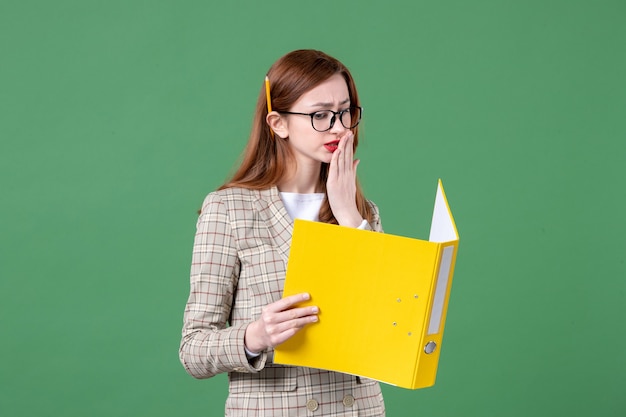 Retrato de maestra leyendo documento amarillo sobre verde