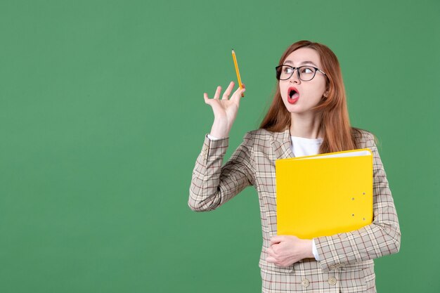 Retrato de maestra posando con archivo amarillo sobre verde