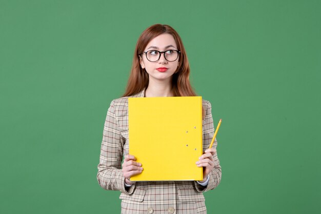 Retrato de maestra sosteniendo archivos amarillos sobre verde