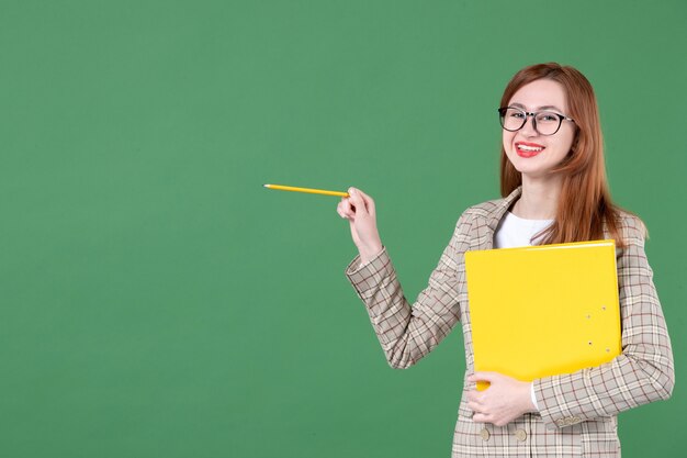 Retrato de maestra sosteniendo felizmente documento amarillo sobre verde