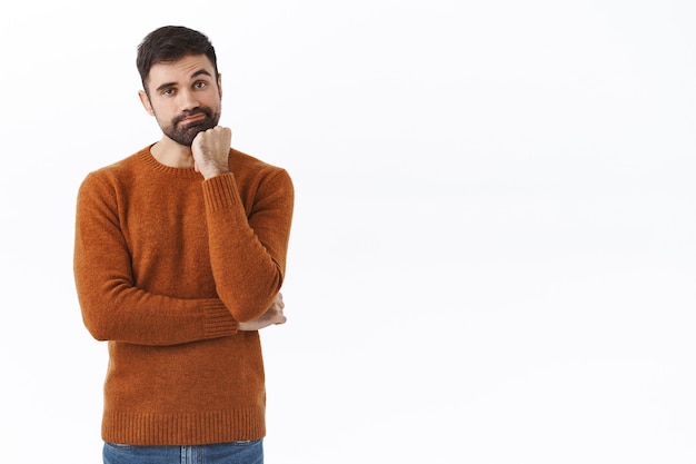 Retrato de marido guapo barbudo aburrido y reacio esperando esposa en el centro comercial mientras compra ropa nueva, sonríe y se apoya en la palma, indiferente, viendo una película aburrida