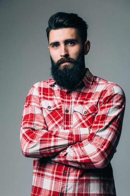 Retrato de masculinidad. Retrato de joven guapo con barba mientras está de pie contra la pared gris