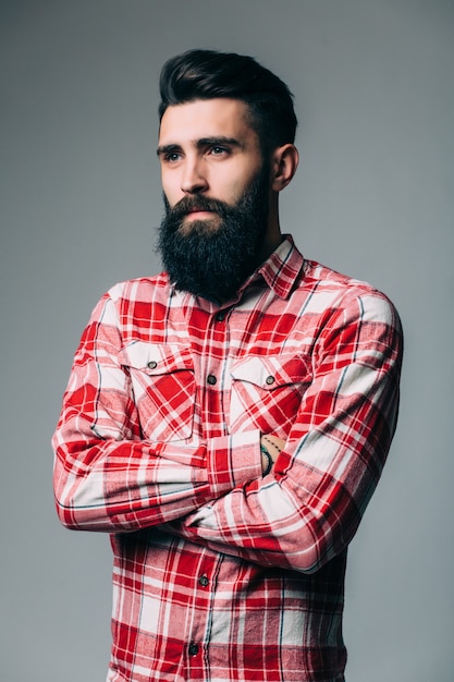 Retrato de masculinidad. Retrato de joven guapo con barba mientras está de pie contra la pared gris