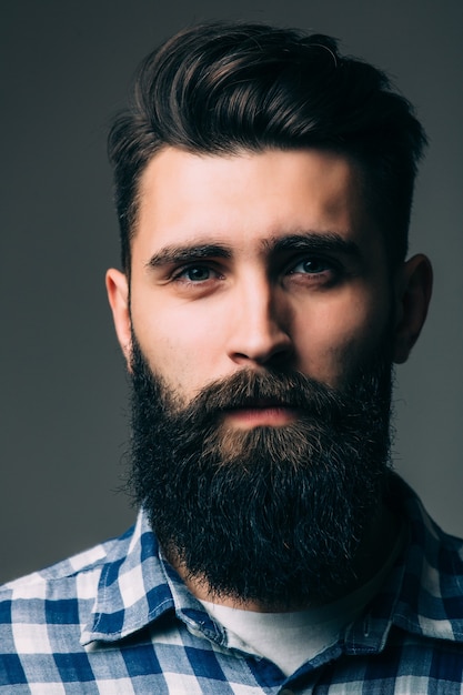 Retrato de masculinidad. Retrato de joven guapo con barba mientras está de pie contra la pared gris