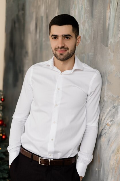 Retrato masculino El hombre moreno hermoso en la camisa blanca y los vaqueros negros con clase presenta en estudio gris