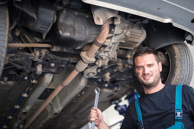 Retrato de mecánico de automóviles con herramienta de llave trabajando debajo del vehículo en el taller de reparación de automóviles
