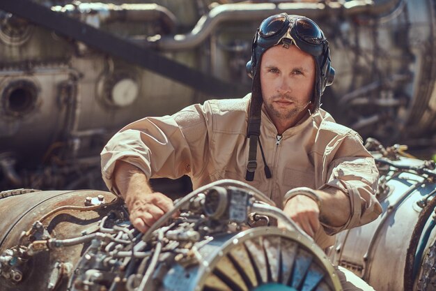 Retrato de un mecánico piloto con uniforme y casco volador, reparando la turbina del avión desmantelada en un museo al aire libre.