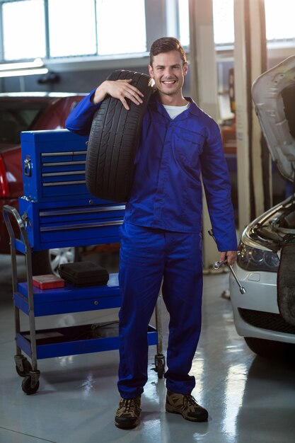 Retrato del mecánico que lleva un neumático