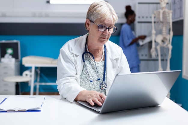 Retrato de médico con estetoscopio usando una computadora portátil para trabajar en el cuidado de la salud en el gabinete. Doctora que trabaja con computadoras y tecnología para hacer análisis de tratamientos de prescripción para su examen.