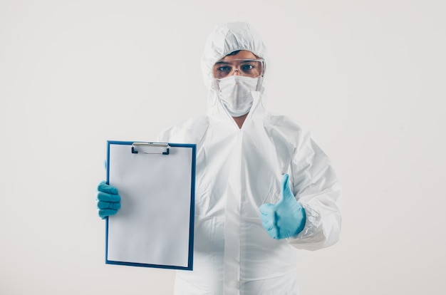 Retrato de un médico en fondo claro con informe médico y pulgares arriba en guantes médicos y traje de protección