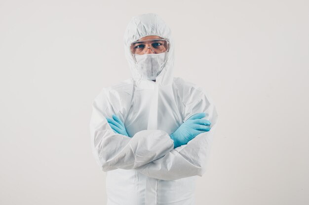 Retrato de un médico en fondo claro de pie y mirando con máscara, guantes médicos y traje de protección