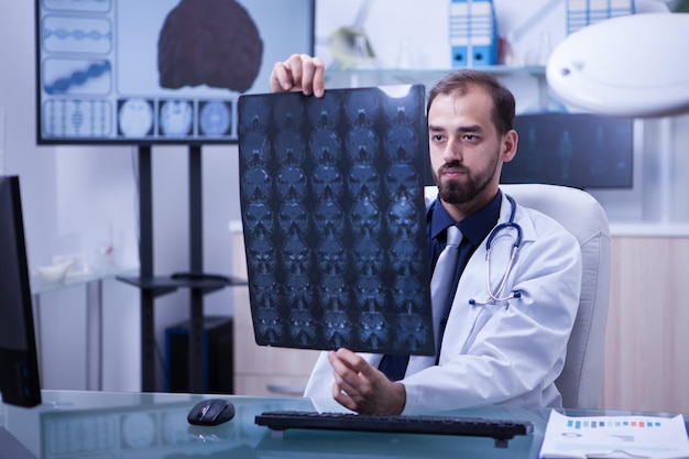 Retrato de un médico joven y ambicioso que examina una radiografía cerebral. Doctor sosteniendo una radiografía de cerebro.